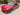 V-style carbon fiber front lip splitter on red sedan front bumper, angled view