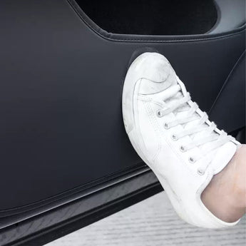 Black door kick protector panel under a white sneaker pressing on the surface