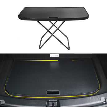 Foldable camping table with black top and folding X legs shown in vehicle trunk