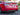 Black carbon fiber rear spoiler with trunk lip on a red sedan, rear view.
