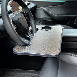 Steering wheel tray desk in car, gray textured board with black mounting lip and edges.